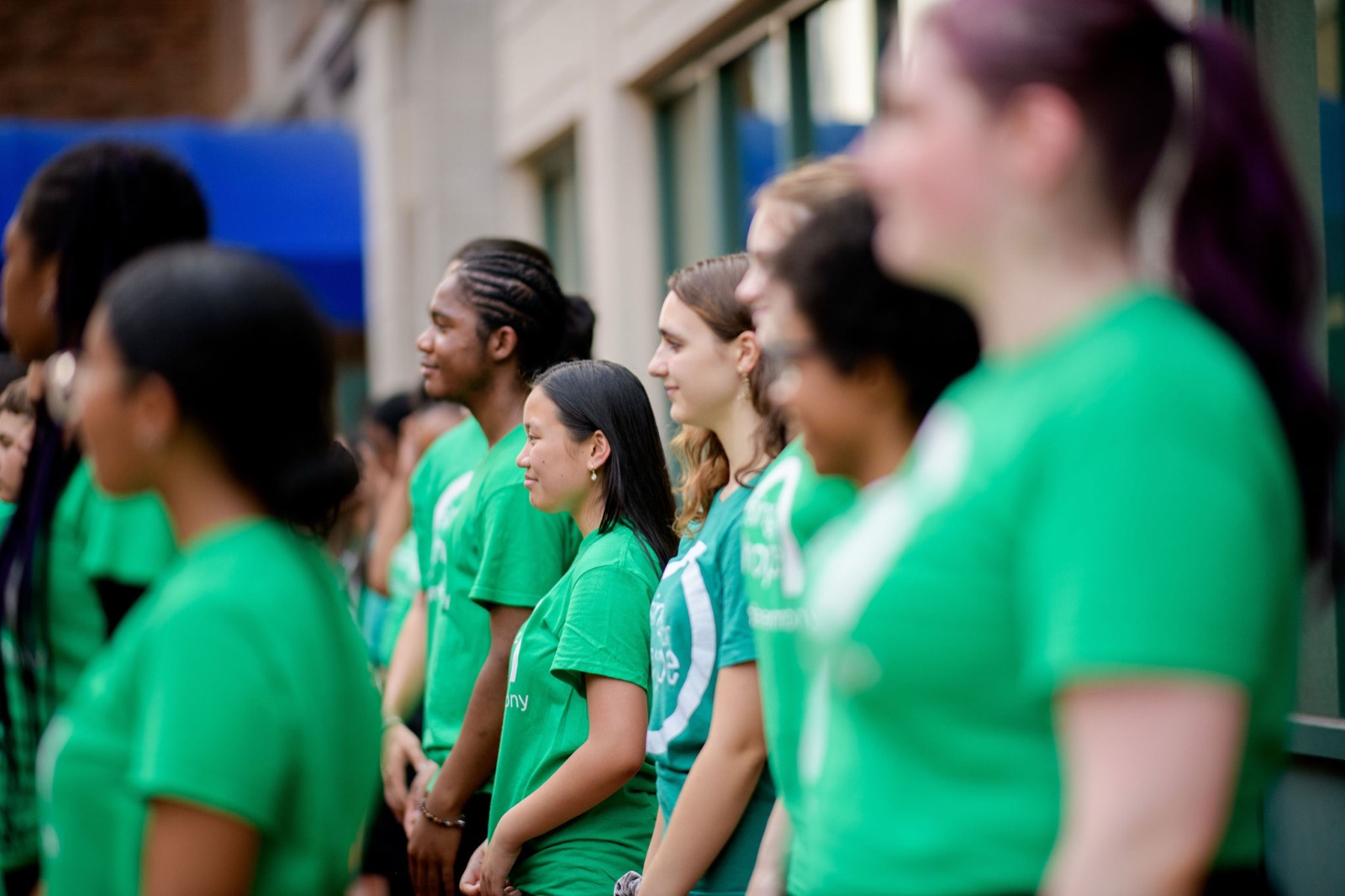 Row of Sing for Hope students in green shirts standing in profile outdoors
