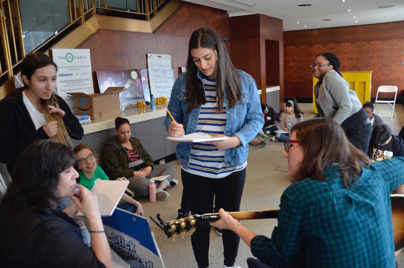 Sing for Hope students writing song lyrics in a circle, one playing guitar