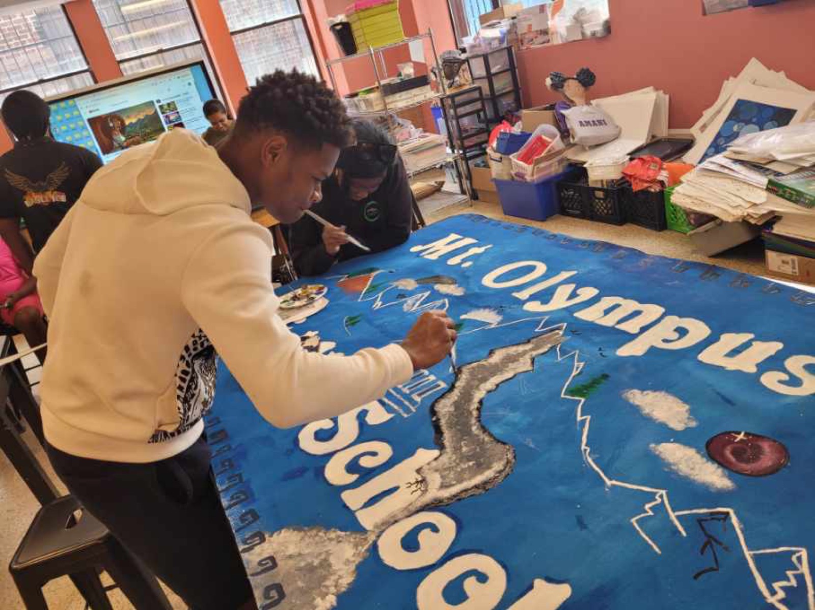 Student painting a large blue ocean mural reading Mt. Olympus School