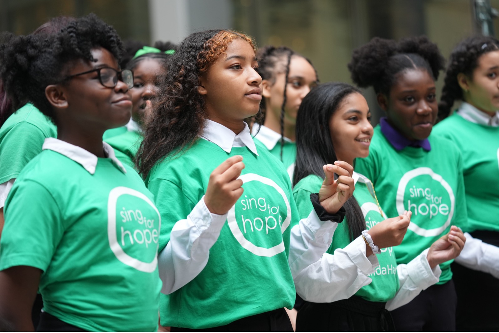 Row of Sing for Hope students in green shirts singing together outdoors